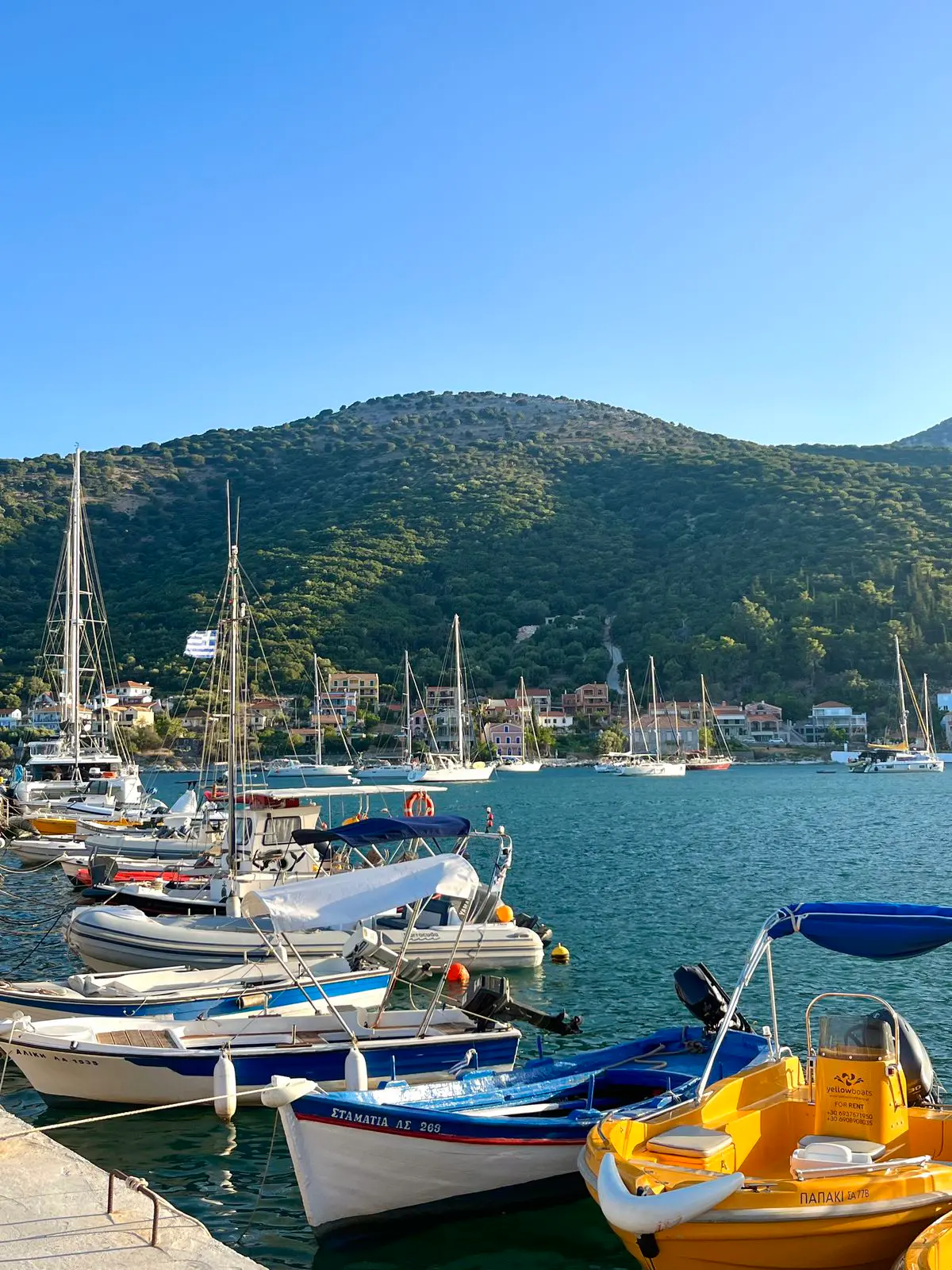 Barcos en el puerto de Agia Efimia, con las casas y una ladera verde de Cefalonia al fondo.